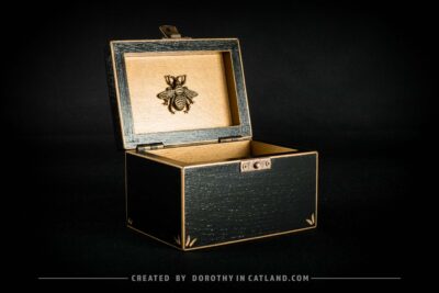 Black wooden jewellery box with a hand-painted golden flower on the lid and a golden bee inside, featuring antique bronze fittings.