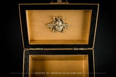 Golden interior of black jewellery box with a detailed golden metal bee ornament