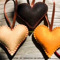 Three felt hearts in black, beige, and yellow colors displayed on a flat surface