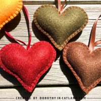 Three handmade felt hearts in green, burgundy, and brown colors lying together