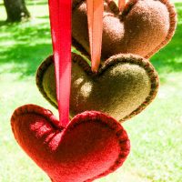 Three felt hearts in green, burgundy, and brown hanging in sunlight