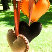 Three felt hearts in black, beige, and yellow hanging in sunlight
