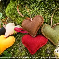 Six handmade felt hearts in autumn colors displayed on green moss