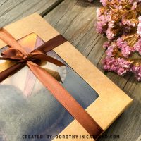 Close-up of autumn felt hearts in a kraft gift box tied with a ribbon, next to dried flowers.